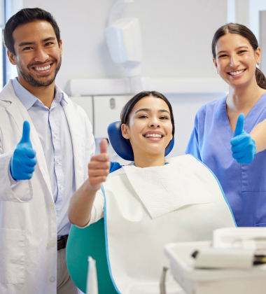 Oral surgeon, dental assistant, and dental patient giving thumbs up